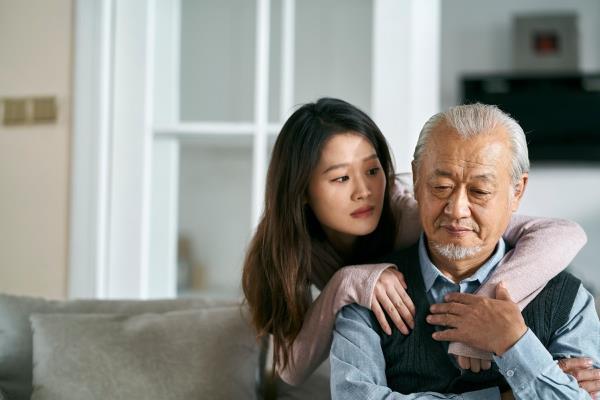 sad senior asian father sitting on couch in living room at home co<em></em>nsoled by adult daughter