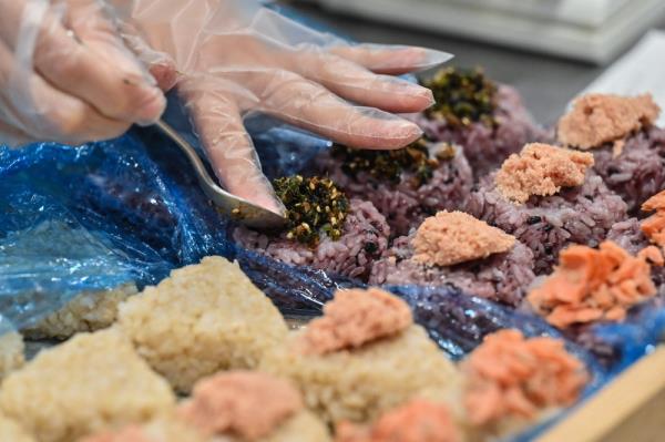 This photo taken on December 6, 2023 shows a staff member placing toppings on rice balls at Taro Tokyo Onigiri, a shop specialising in Japanese rice balls, known as 